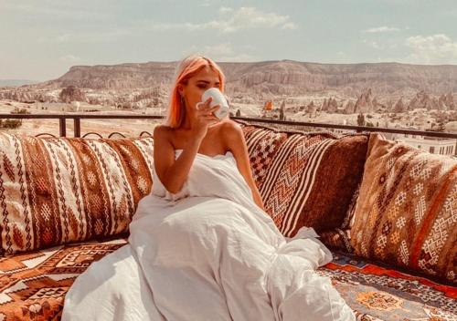 a woman in a white dress sitting on a couch with a cup at Osmanli Cappadocia Hotel in Göreme