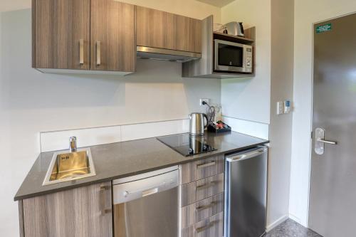 a kitchen with wooden cabinets and a stainless steel appliance at Ramada Suites by Wyndham Queenstown Remarkables Park in Queenstown