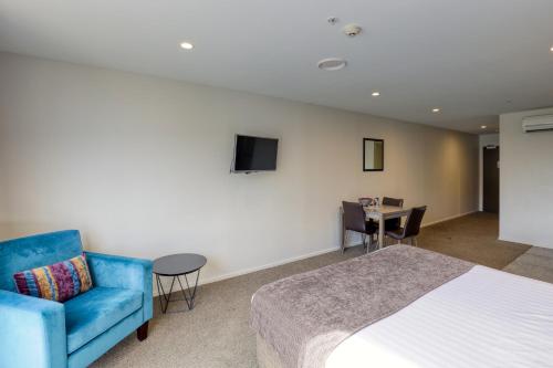 a bedroom with a bed and a blue couch and a table at Ramada Suites by Wyndham Queenstown Remarkables Park in Queenstown