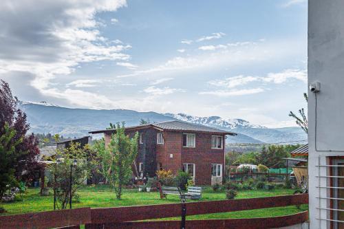 una casa de ladrillo con una valla y montañas en el fondo en Temporario Patagonia en El Bolsón