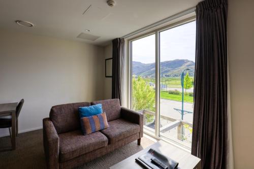 a living room with a couch and a large window at Ramada Suites by Wyndham Queenstown Remarkables Park in Queenstown