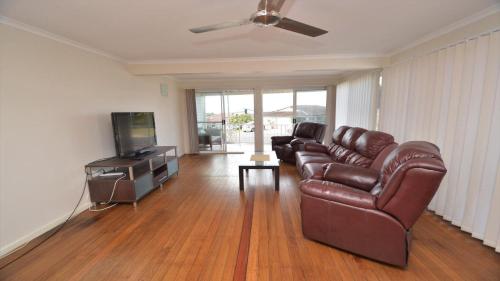 a living room with a leather couch and a television at 1 5 Pilot Street Yamba in Yamba