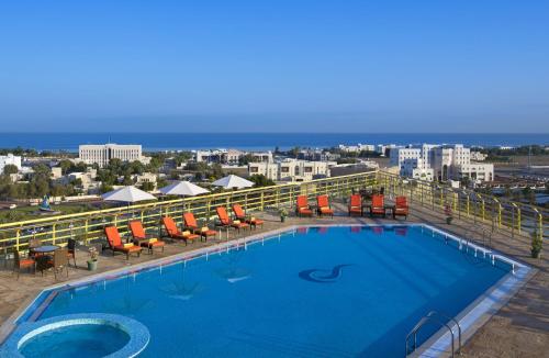 a beach with a pool, chairs, and a pool table at City Seasons Hotel & Suites Muscat in Muscat