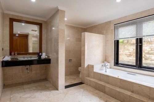 baño con bañera, lavabo y ventana en Jimbarwana Hotel, en Negara