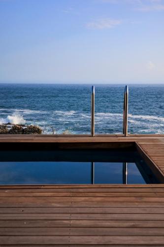 a view of the ocean from a house with a pool at OnTheRocksBB Solar Powered Guesthouse and Ocean Lodge in Bettyʼs Bay
