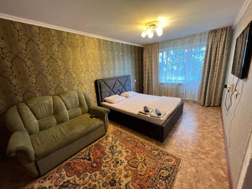 a bedroom with a bed and a couch and a window at Стандарт Камзина 74 г. Павлодар in Pavlodar