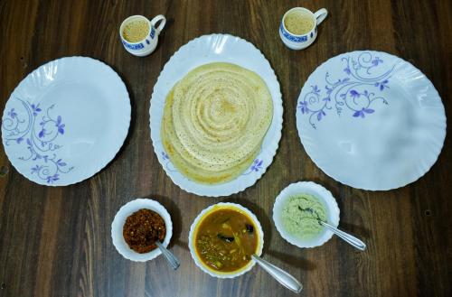 a table topped with white plates and bowls of food at Raymond's Holiday Homes in Vythiri