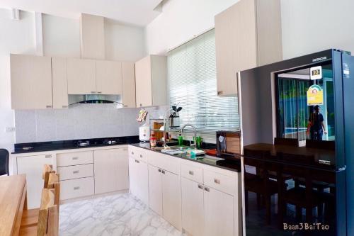 a kitchen with white cabinets and a black refrigerator at Siri Nathai Pool Villa สิรินาไทย พูลวิลล่า in Krabi town