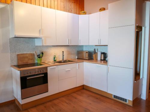 uma cozinha com armários brancos e um forno com placa de fogão em Apartment Cassiopée 26 by Interhome em Les Rasses