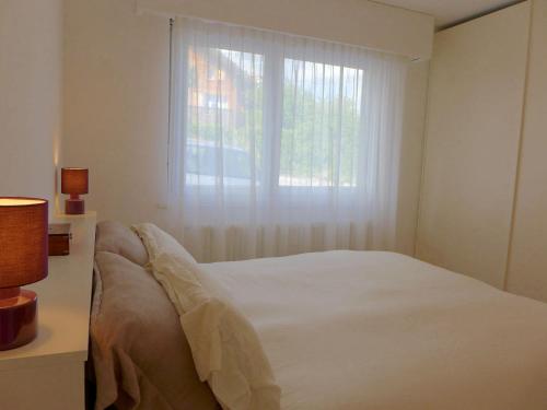 a white bedroom with a bed and a window at Apartment Clair-Azur-3 by Interhome in Crans-Montana