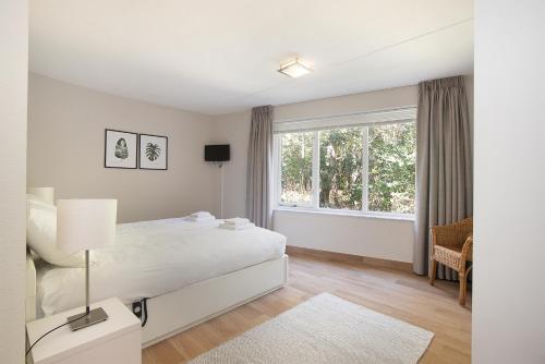 a white bedroom with a bed and a window at Hello Zeeland - Appartement Loverendale 10 in Domburg
