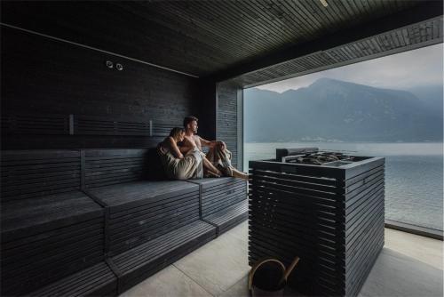 a man sitting on a couch in a room with a view of the ocean at EALA My Lakeside Dream - Adults Friendly in Limone sul Garda