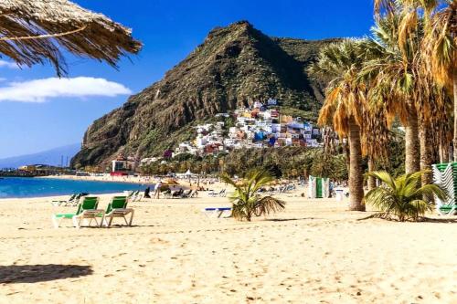 una playa con palmeras y sillas y una montaña en Vacanze da sogno, en San Miguel de Abona