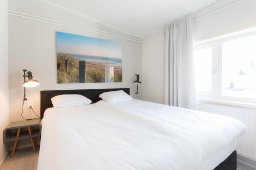 a white bedroom with a large white bed and a window at Hello Zeeland - Appartement Beatrixstraat 29 in Domburg