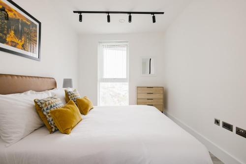 a white bedroom with a large bed with yellow pillows at CitySpace Acton in London