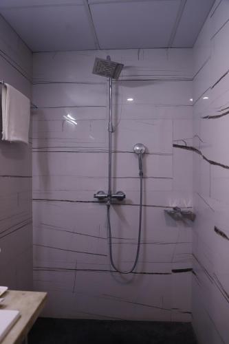 a shower in a bathroom with white tiles at The Jamun Tree in Muzaffarpur