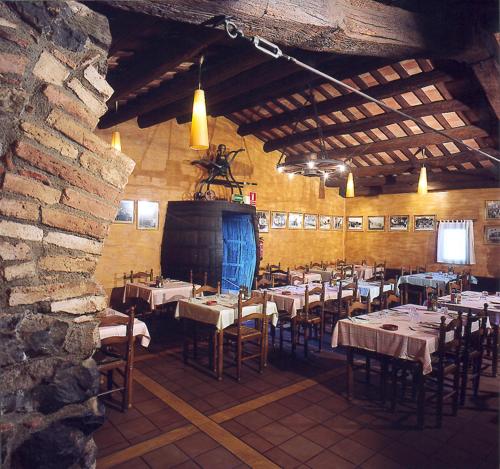 Hostal Mallorquines في Riudarenes: غرفة طعام بها طاولات وكراسي وجدار حجري