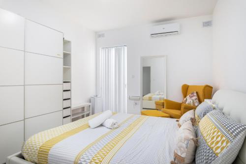 a white bedroom with a bed and a yellow chair at Spacious, Modern & Cosy 2 Bedroom 2 Bathroom Apartment - St. Julians in St. Julianʼs