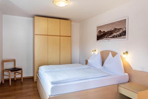 a bedroom with a white bed and a chair at Villa Erina App D2 in Ortisei