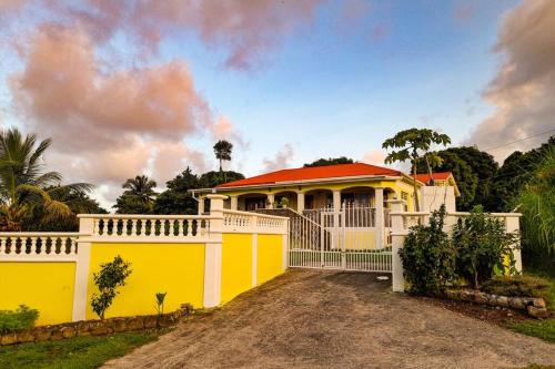 a yellow house with a white fence in front of it at Sunrise Bliss Villa with Hot Tub, King Bed, Ocean, and Mountain View in La Plaine