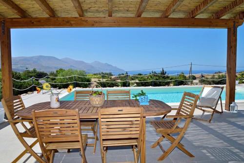una mesa de madera y sillas en un patio con piscina en Villa Occidente - Homelike Villas, en Castellammare del Golfo