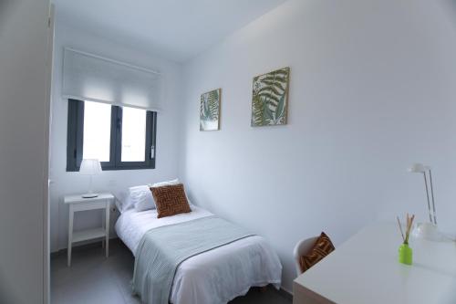Habitación blanca con cama y escritorio en RentalSevilla Apartamento luminoso 2 dormitorios, en Sevilla