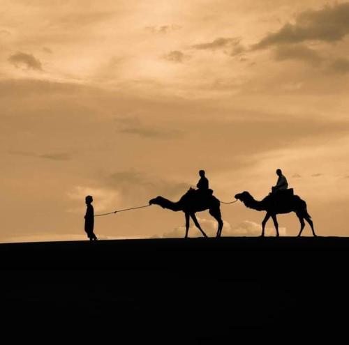 dos personas montando camellos frente a la puesta de sol en Ahlam Luxury Camp, en Merzouga