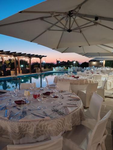 a table with white tables and chairs and a pool at Hotel Donna Carmela Sede Unica a Sciacca in Sciacca