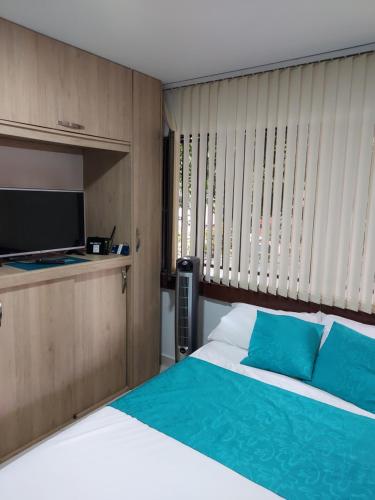 1 dormitorio con 1 cama con almohadas azules y TV en Apartaestudio Laureles - Viva Laureles, en Medellín