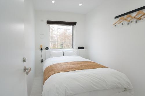 a white bedroom with a large bed and a window at NISEKO EPIC HOUSE in Niseko