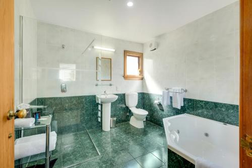 a bathroom with a sink and a toilet and a tub at Harrogate Gardens Motel in Hanmer Springs