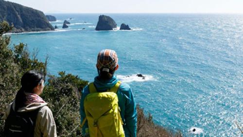 two people standing on a cliff looking at the ocean at Kyukamura Minami-Izu in Minamiizu