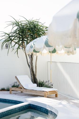 a pool with a table and an umbrella and a palm tree at Motel Molly - Boutique Hotel Mollymook in Mollymook