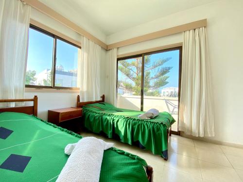 een slaapkamer met 2 groene bedden en een groot raam bij Kaan Hotel & Apartment in Kyrenia