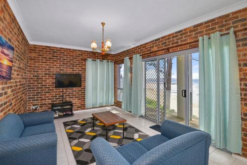 a living room with blue chairs and a brick wall at Beachside at The Entrance in The Entrance