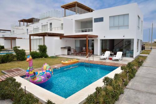 a house with a swimming pool in front of a house at Casa de playa: Disfruta de grandes momentos y del sol todo el año en Paracas in Paracas