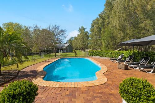 a swimming pool in a yard with chairs and an umbrella at The Convent Hunter Valley Hotel in Pokolbin