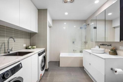 a white kitchen with a sink and a washing machine at Sandy@Village - newly renovated + bay views in Sandringham