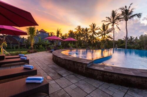 a pool at a resort with tables and umbrellas at Uma Dawa Resort and Spa in Ubud