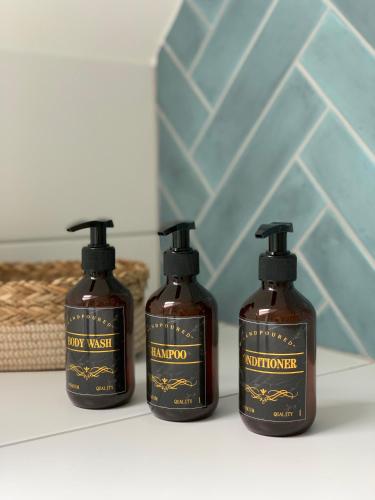 3 bouteilles de shampoing et d'après-shampoing assises sur un comptoir de salle de bains dans l'établissement Appartements Le Tilleul de la Vallée Noble, à Westhalten