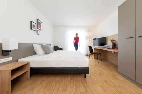 ein Schlafzimmer mit einem Bett und eine Frau am Fenster in der Unterkunft Brera Serviced Apartments Stuttgart in Stuttgart