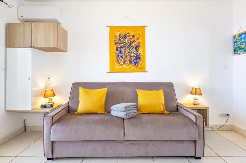 a couch with two yellow pillows in a living room at Océanides - studio rénové avec magnifique vue mer - Saint-Gilles-Les-Bains in Saint-Gilles les Bains