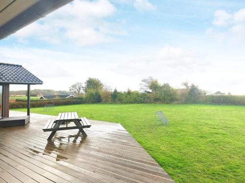 eine Holzterrasse mit einem Picknicktisch und einem grünen Feld in der Unterkunft 10 person holiday home in Faaborg in Bøjden