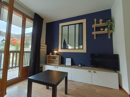 un salon avec un mur bleu, une table et une télévision dans l'établissement Snowliday - Appartement Rénové en résidence 4* pour 4 pers. Valmeinier 1900, à Valmeinier