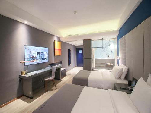a hotel room with two beds and a desk at LanOu Hotel Zhangye Hexi College Ganquan Park in Zhangye