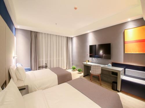 a hotel room with two beds and a desk and a television at LanOu Hotel Zhangye Hexi College Ganquan Park in Zhangye