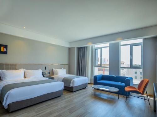 um quarto de hotel com duas camas e um sofá azul em LanOu Hotel Zhongning Weimin City Plaza em Jiangoushan