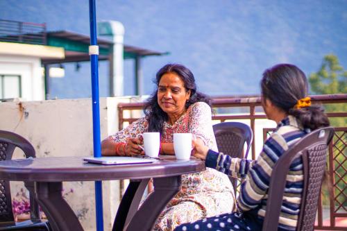 two women sitting at a table with coffee cups at Triple One Hotel Tapovan Rishikesh,Near Laxman Jhula in Rishīkesh
