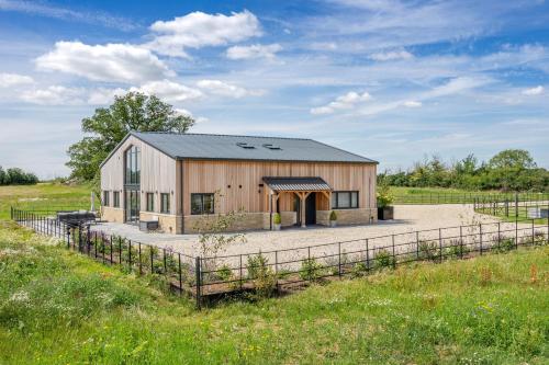 a wooden barn with a fence in a field at The Grove - Converted Cattle Barn in Malmesbury