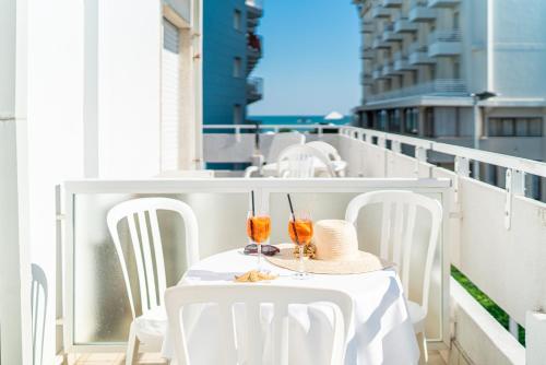 un tavolo bianco con due bicchieri e un cappello sul balcone di Hotel Pigalle a Lido di Jesolo